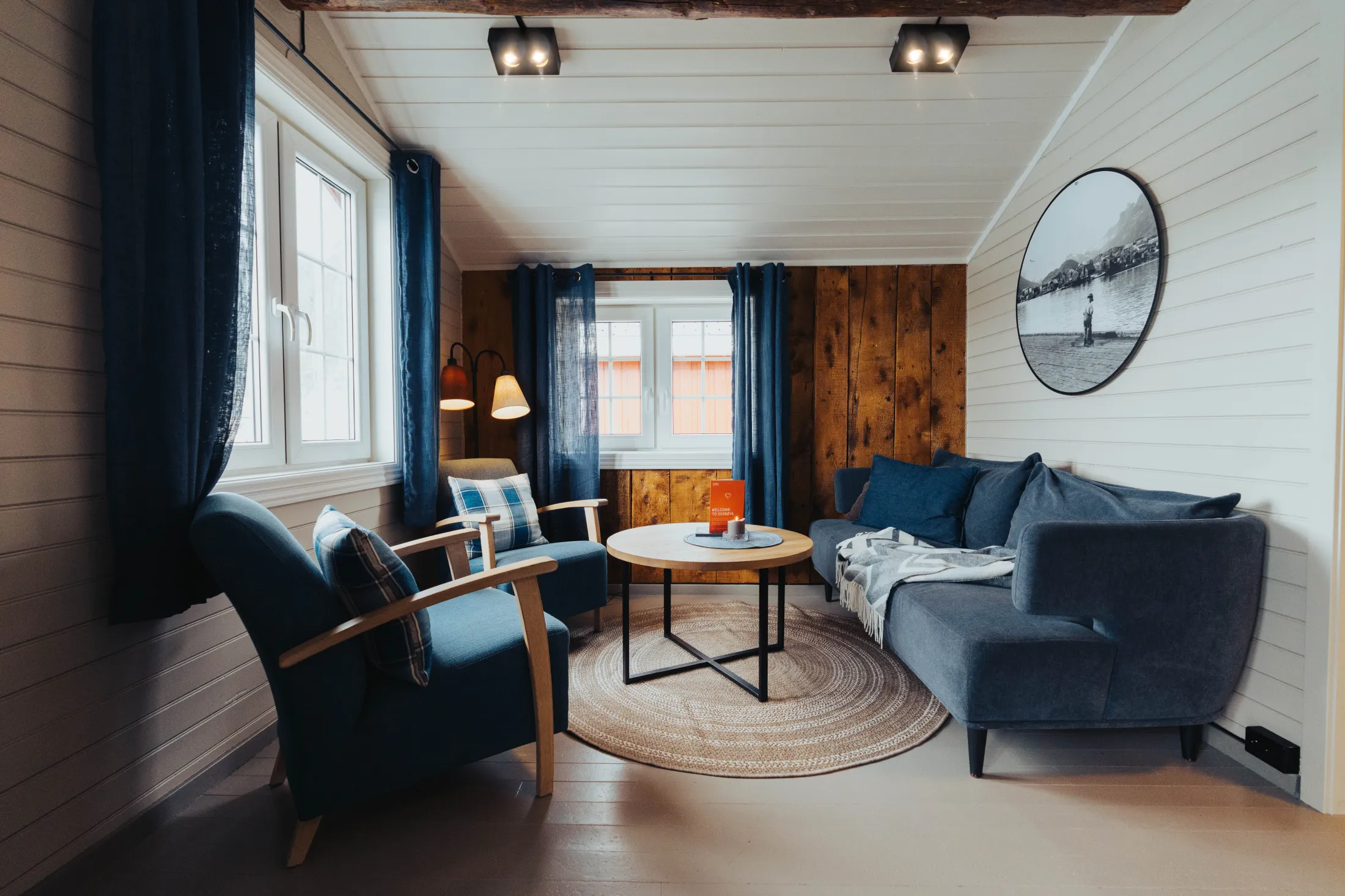 Living room with light flooring, white ceiling and floors, a blue sofa, two armchairs, a coffee table, and an accent wall featuring reclaimed wood.
