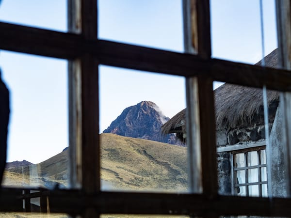 A view of a mountain through a multi-pane wooden window of an old stone building.