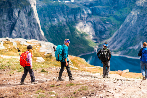 Four hikers walking on a mountain trail with a deep valley and water in the background.