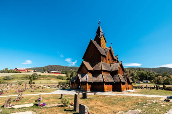 Heddal Stave Church in Norway under a clear blue sky, surrounded by a graveyard and hills.