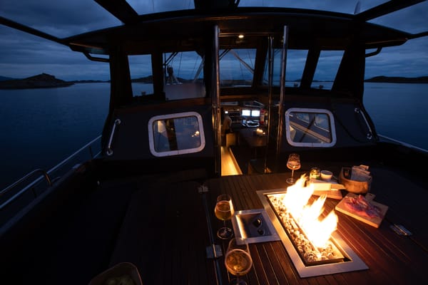 Looking from inside the stern of a boat over a table with a small fire pit at dusk.