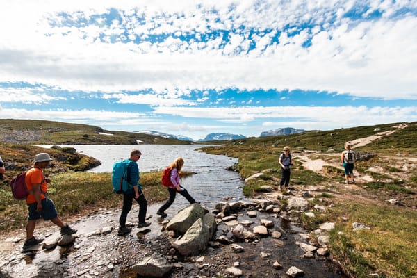 A group of hikers walking on a trail near a lake under a blue sky with scattered clouds.