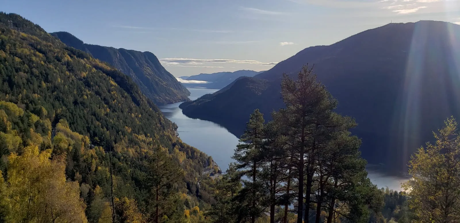 Scenic view of a deep fjord framed by steep mountains, with sunlight catching the water in the distance.