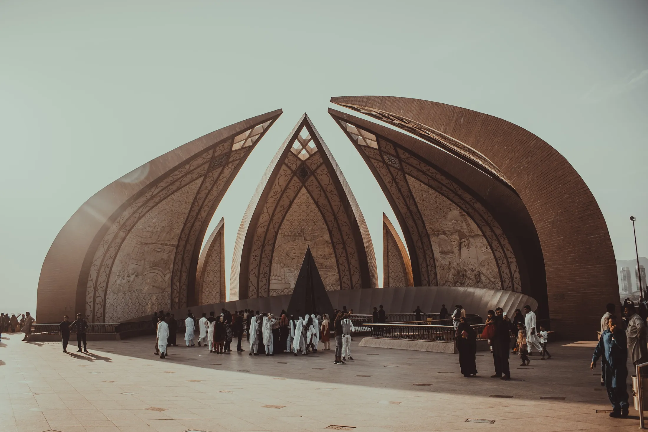 Visitors walk around the petal-shaped granite structures of the Pakistan Monument under a bright, hazy sky in Islamabad.