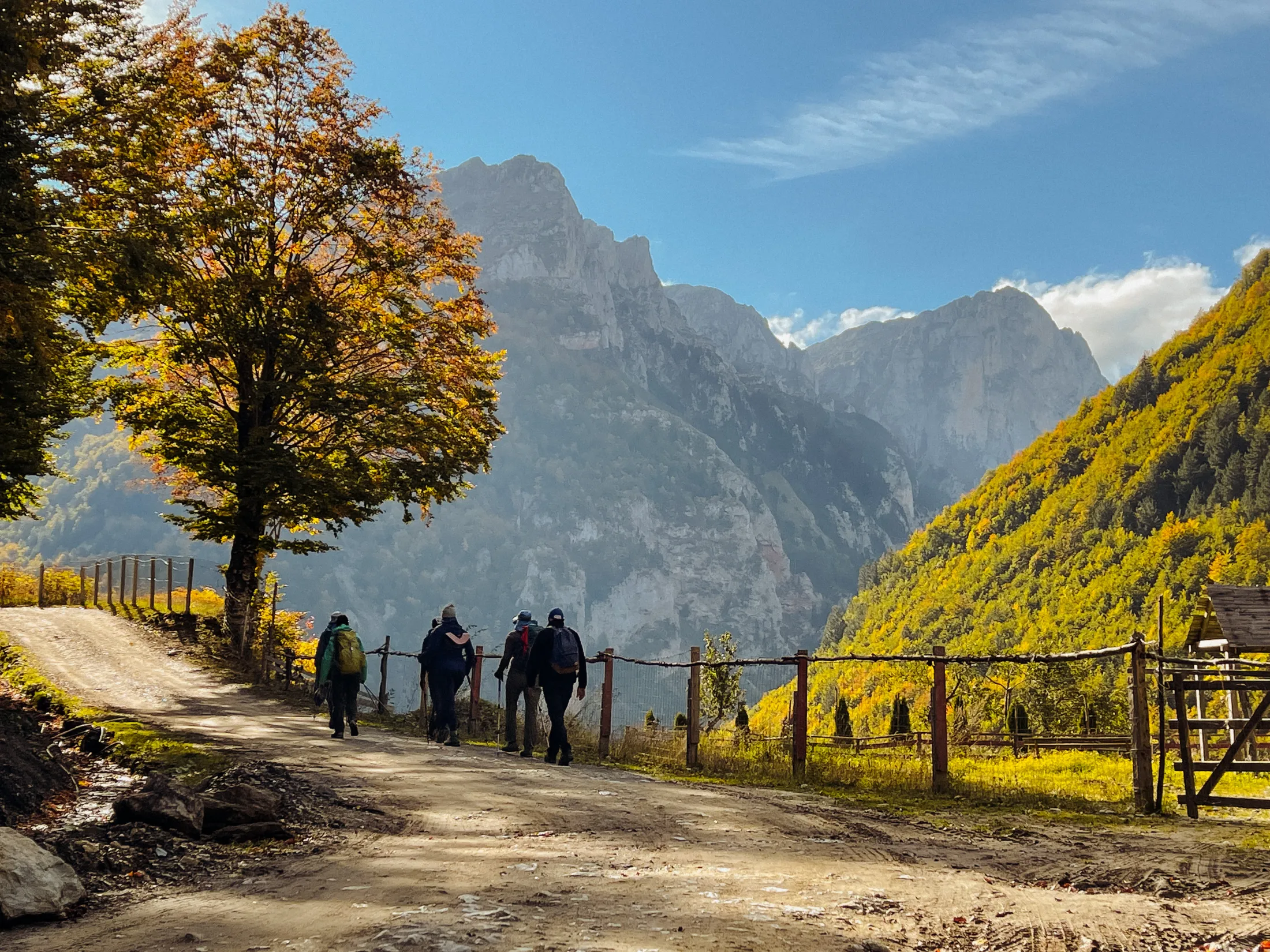 Hikers walking on a dirt path with mountain views and autumn trees.