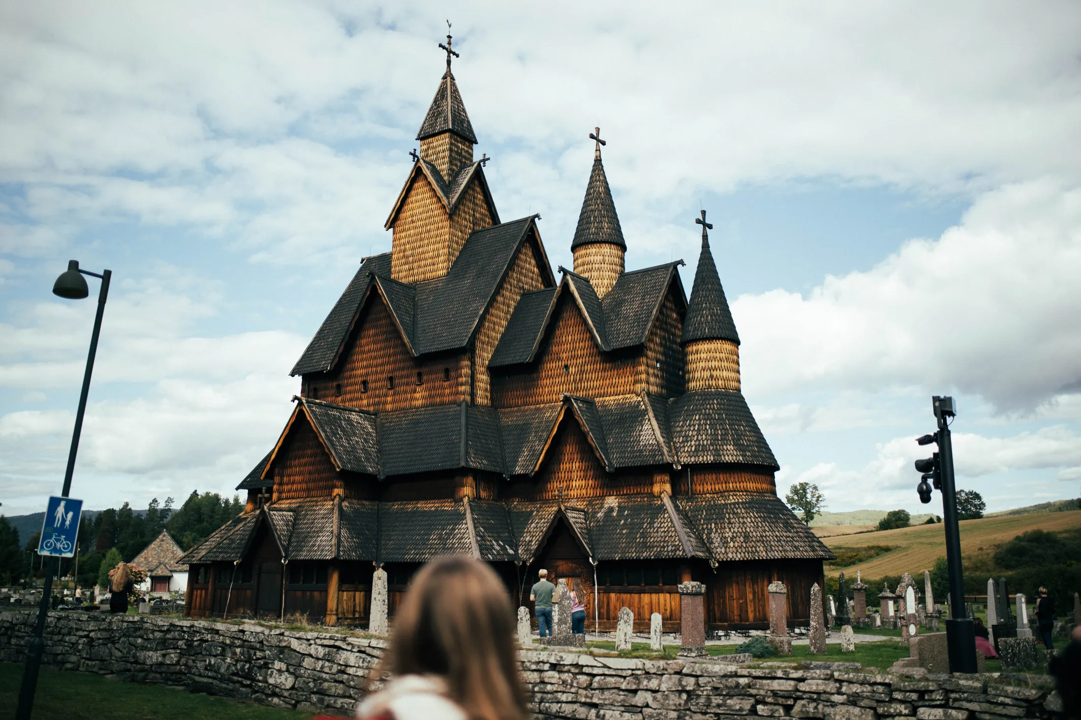 A traditional wooden stave church with dark shingled roofs under a cloudy sky.