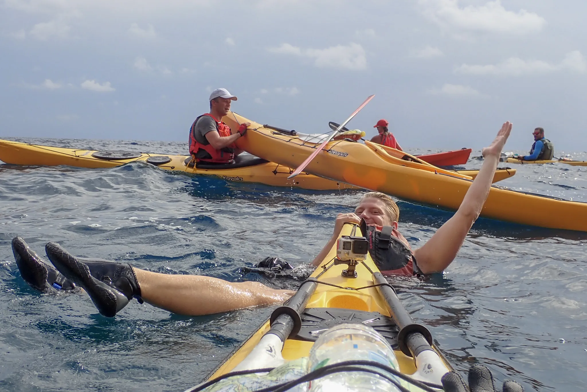 A kayaker smiles and waves while floating in the water beside their kayak in the ocean.