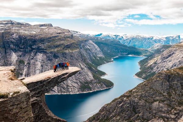 Hikers standing on Trolltunga rock jutting out over a scenic fjord and mountains in Norway.