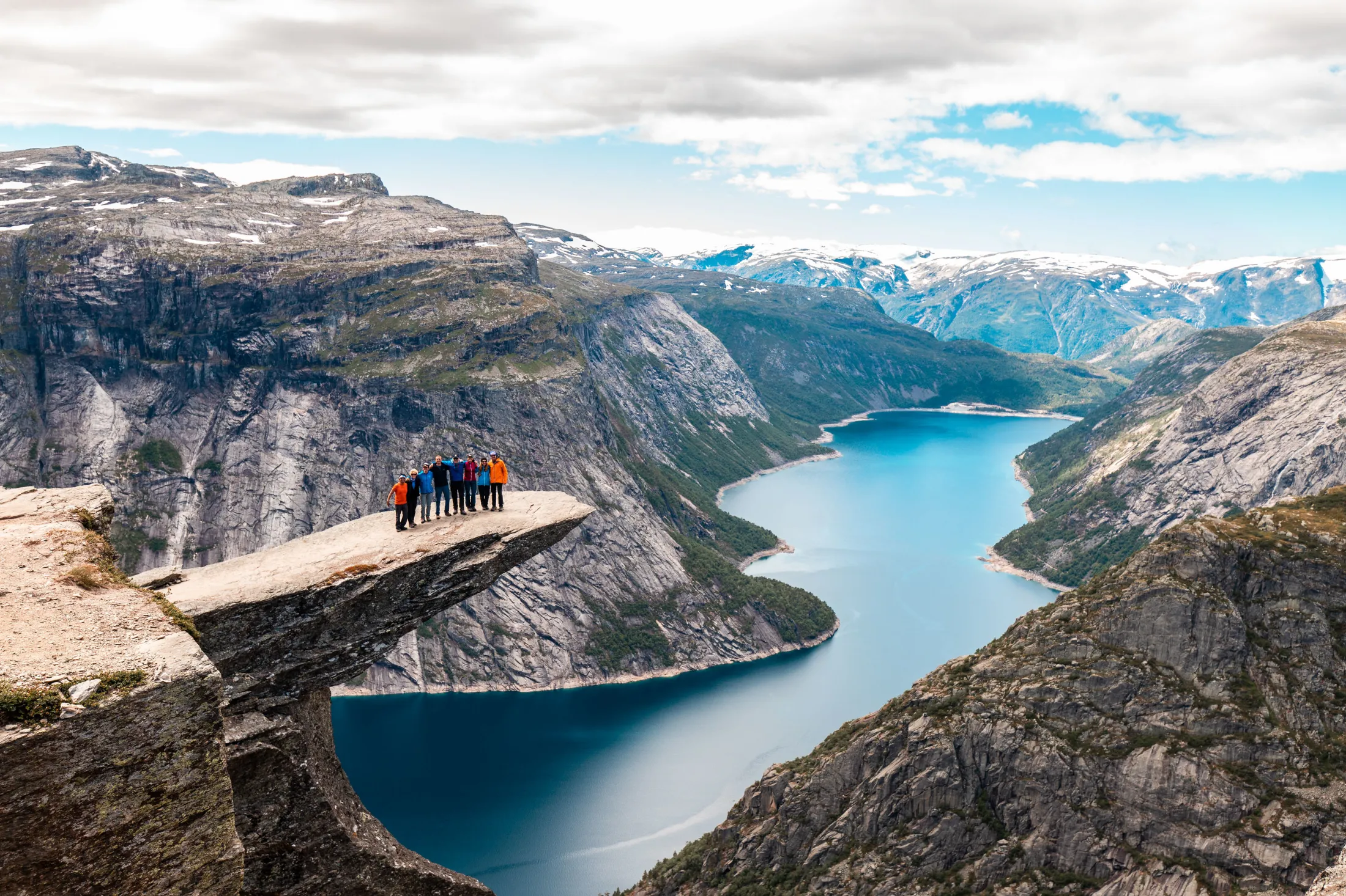 Hikers standing on Trolltunga rock jutting out over a blue fjord in Norway.
