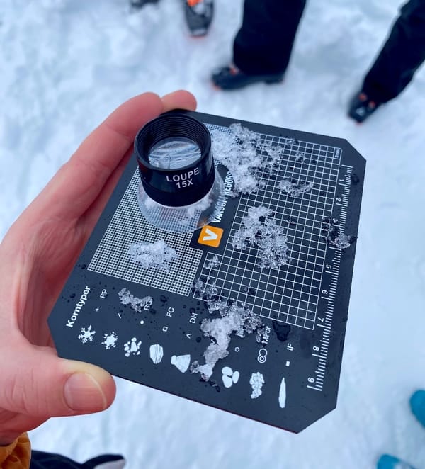 A person holds an avalanche crystal analysis card with a magnifying glass and snow samples on it.