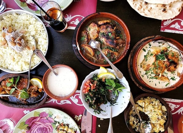 An overhead view of a table spread with traditional meze dishes, including rice, roasted chicken, salad, sauces, and fresh flatbread.