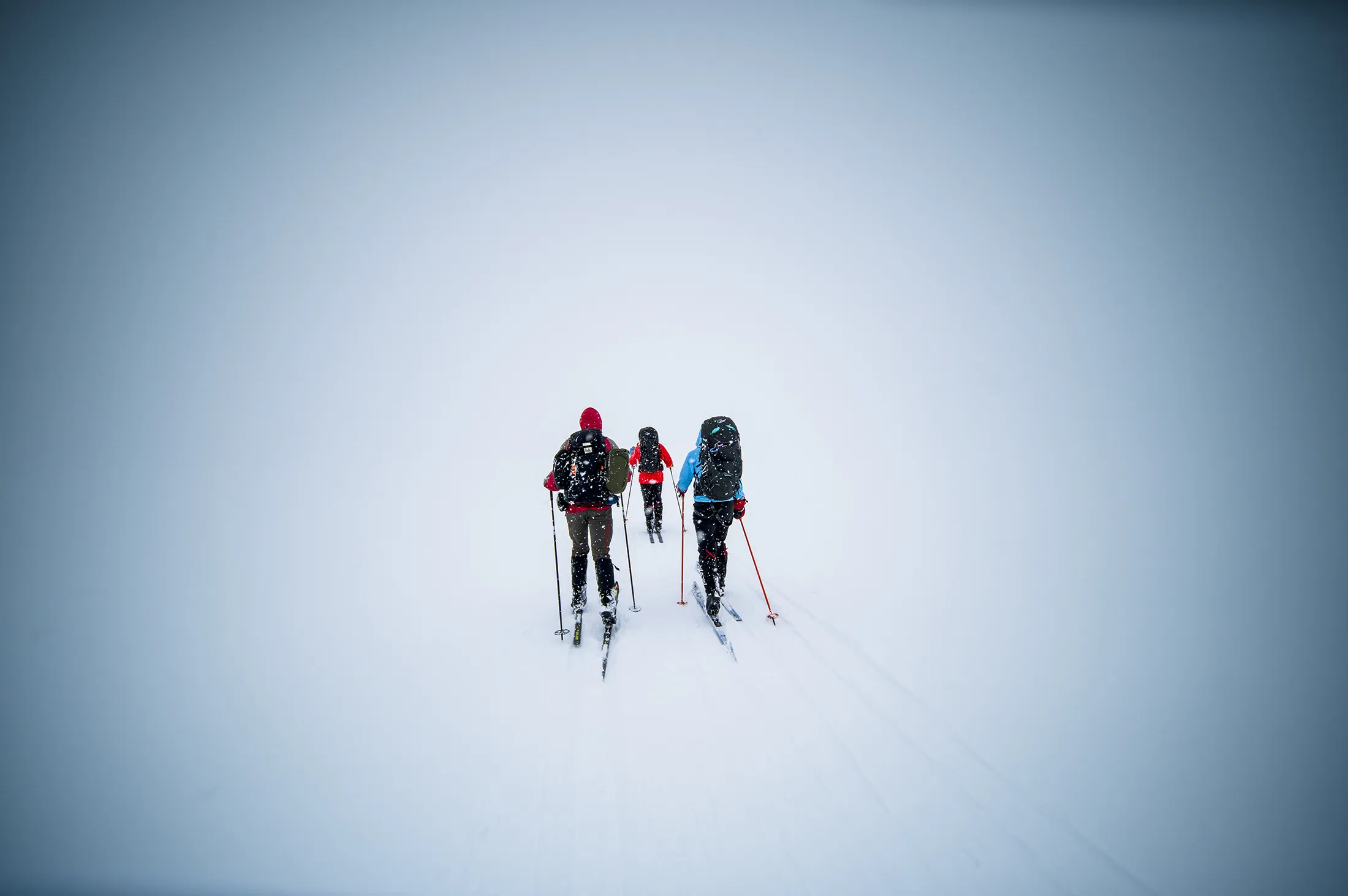 Three cross-country skiers wearing backpacks skiing across a vast snow-covered landscape.