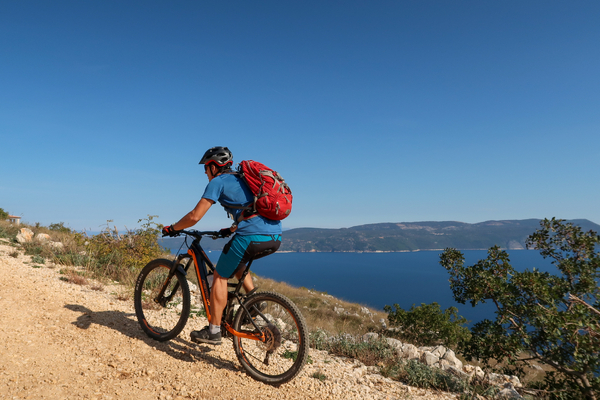 A cyclist on a mountain bike riding uphill along a coastal path overlooking the sea.