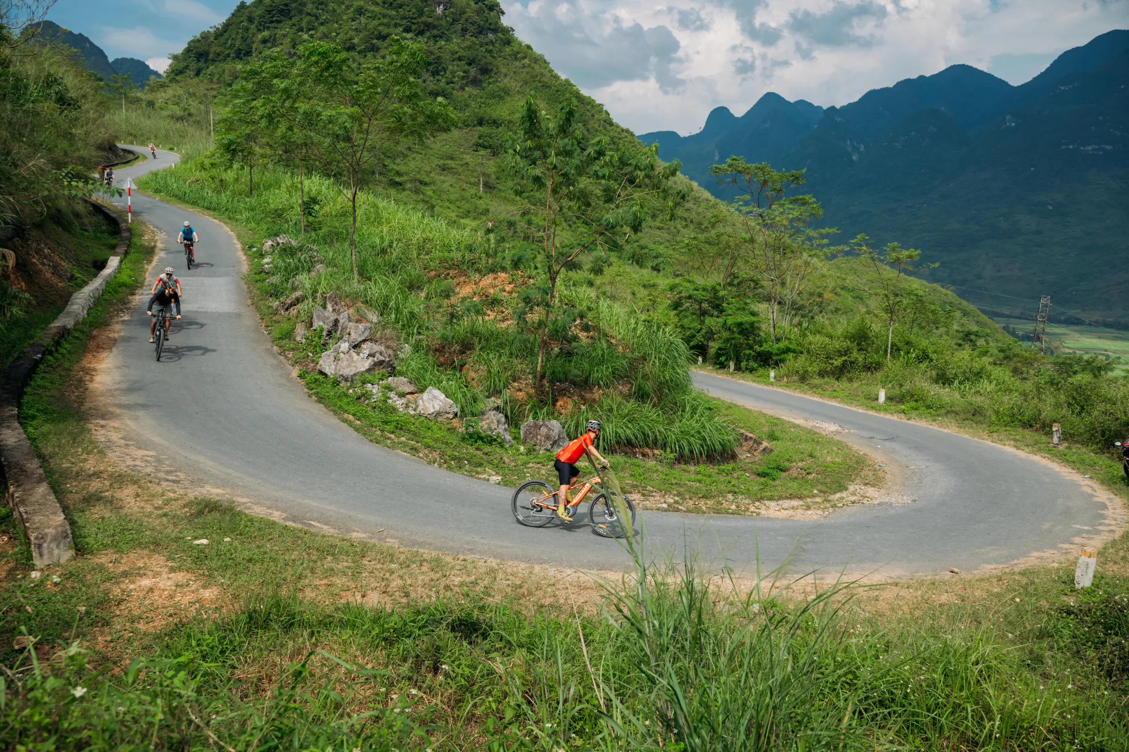 Cyclists riding along a winding mountain road in a lush, green landscape.