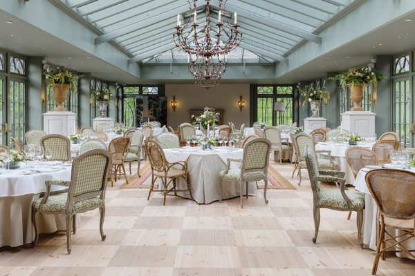 A spacious, elegant dining conservatory with round tables, chairs, large chandelier, and glass roof.