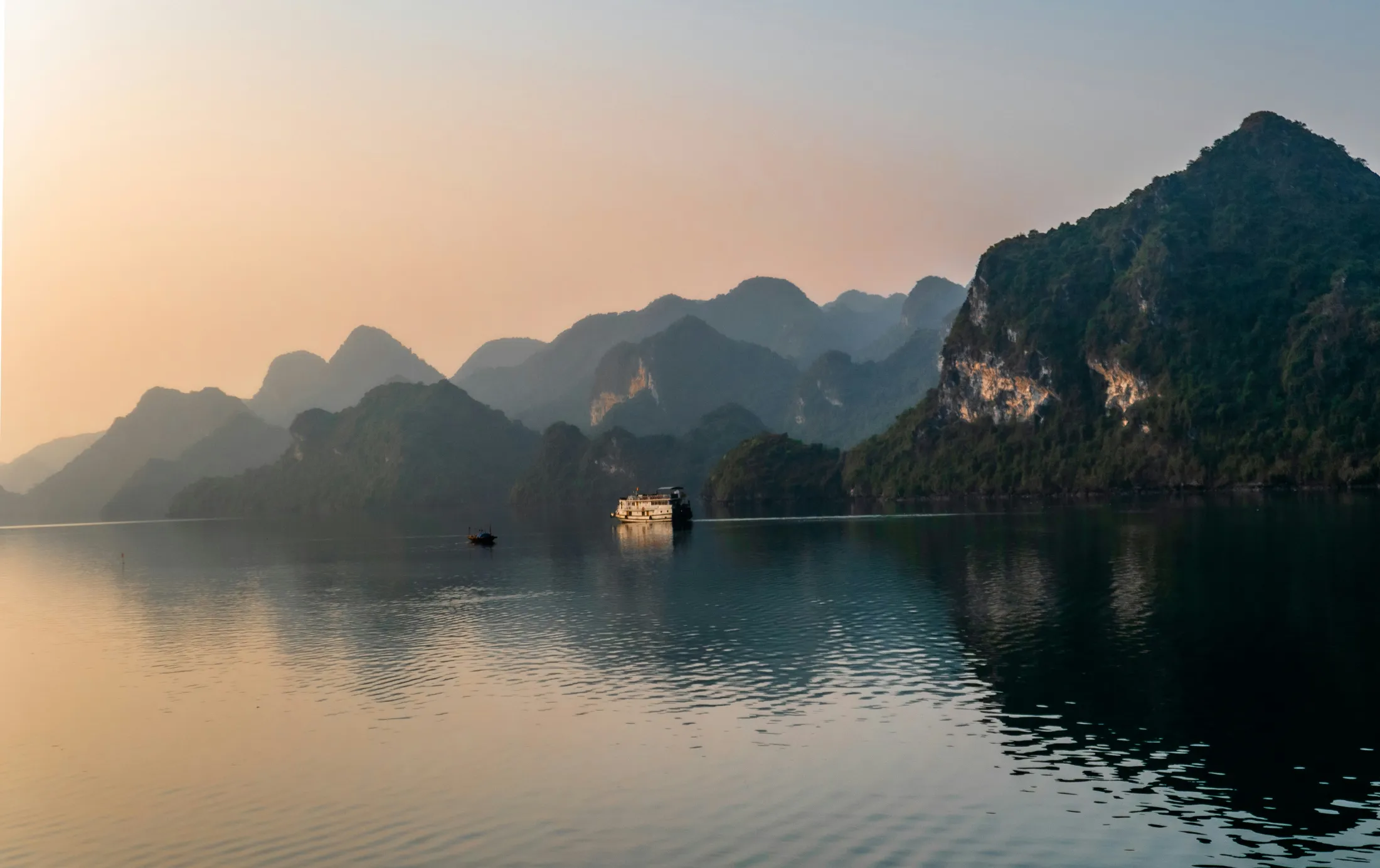 A boat on a calm lake surrounded by karst mountains at dusk.