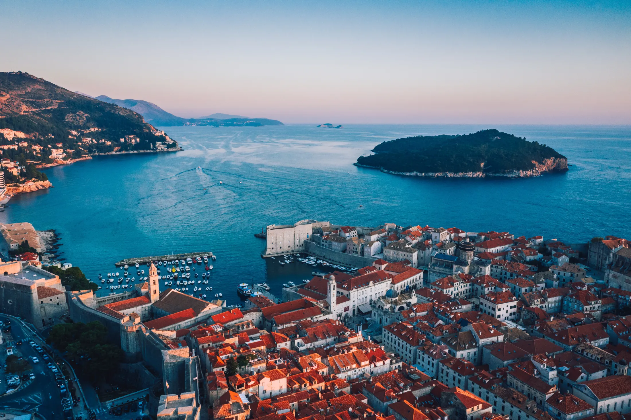 View of the Dubrovnik coastline with white houses and a historic fortress bathed in the golden light of a sunrise.