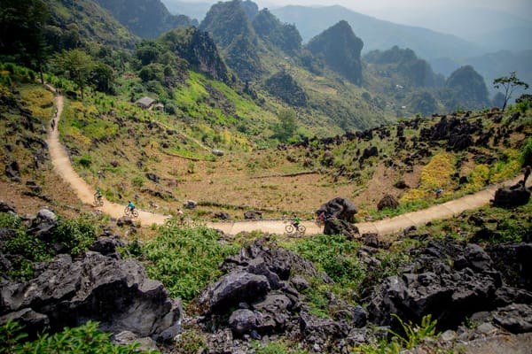 A winding dirt path cutting through a rocky mountain valley with steep peaks in the background.