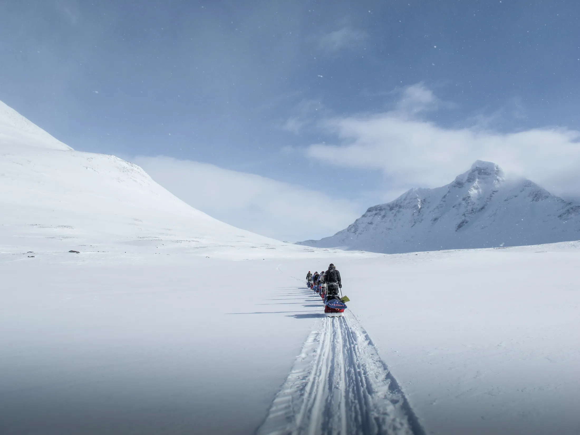 A person riding a snowmobile on a snowy plain with distant mountains under a blue sky.