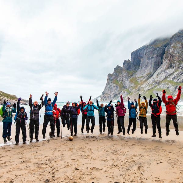 A bunch of people jumping excitedly up in the air on a rainy day at a beach.