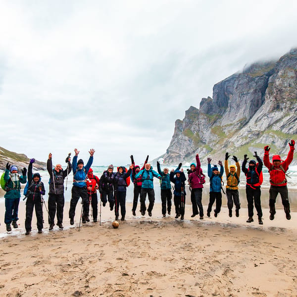A group of happy hikers enjoying a jump at a beach sorrounded by mountains