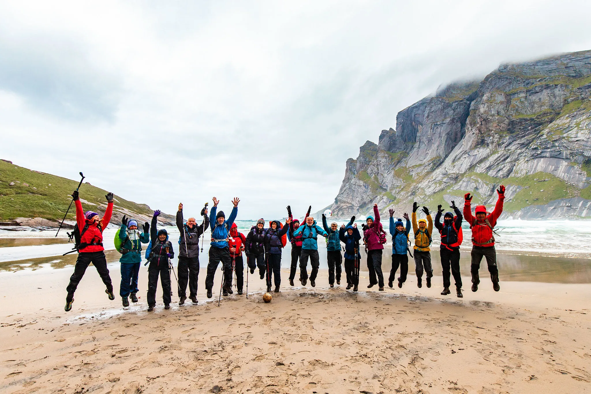 Happy hikers enjoying a jump on a beach sorrounded by mountains