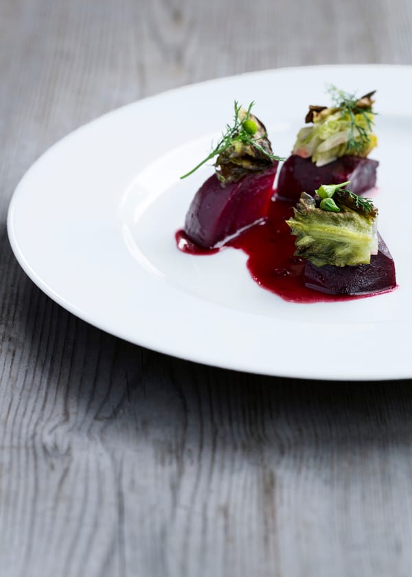 Three pieces of beetroot topped with salad and red sauce on a white plate.