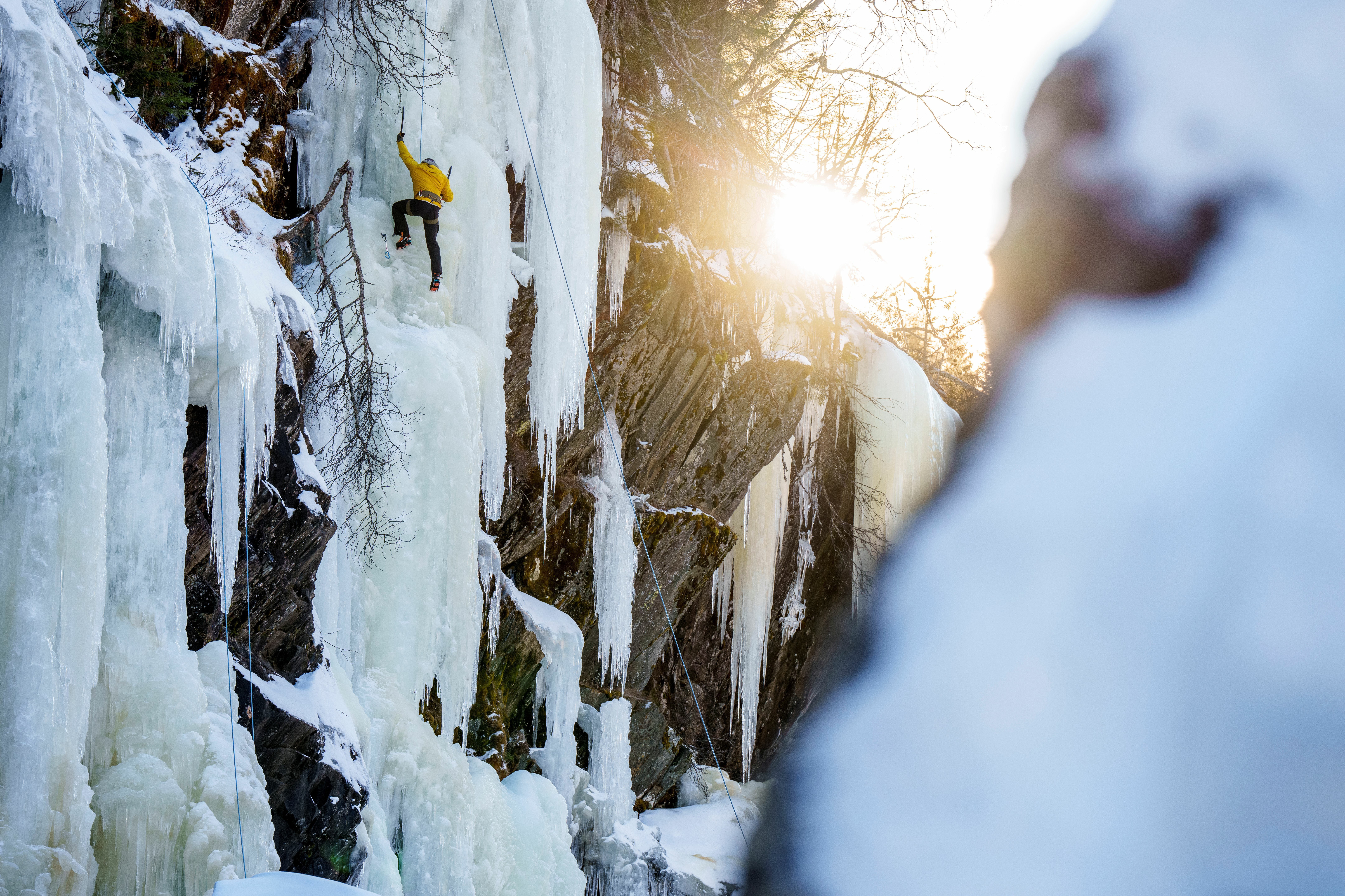 Ice climber in action on an ice waterfall and the sun