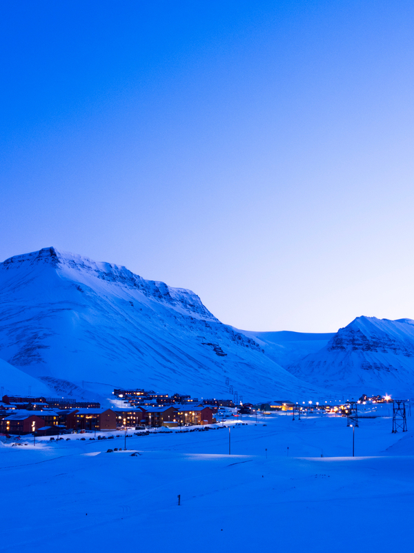 Snowy mountains at dusk colored blue by the light with some houses