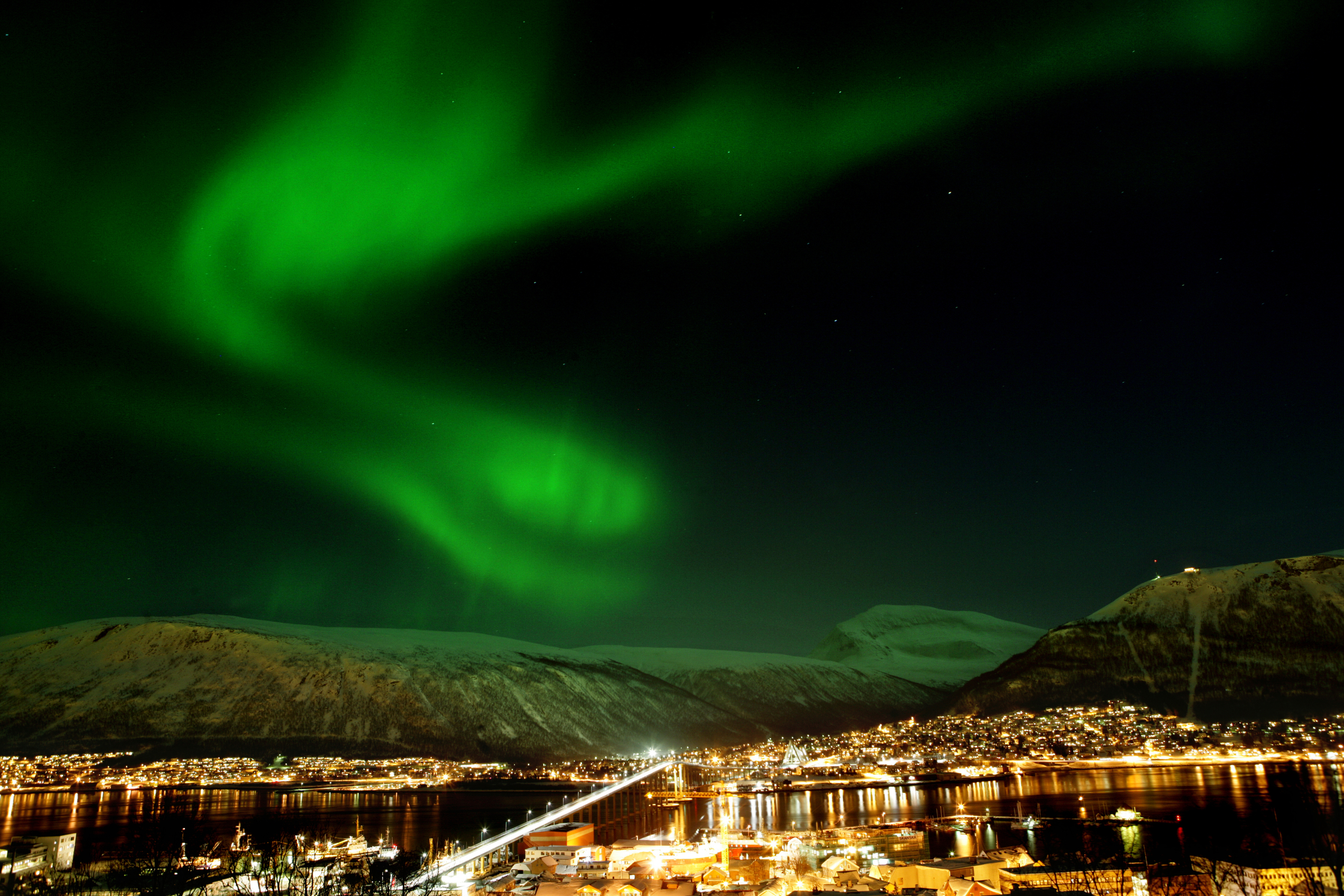 Northern lights over a city and snowy mountains