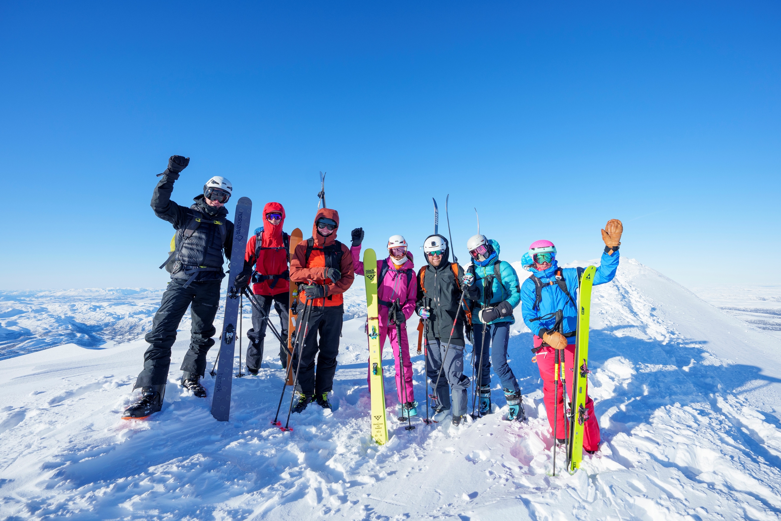 Group of skiers standing on top of a mountain with blue skies