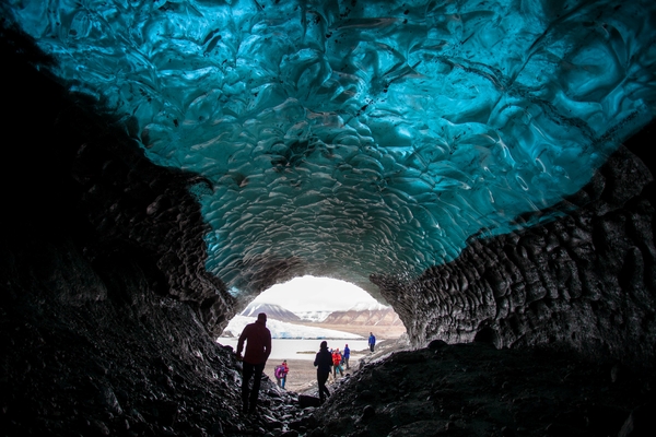 A cave under a glacier with people walking through it