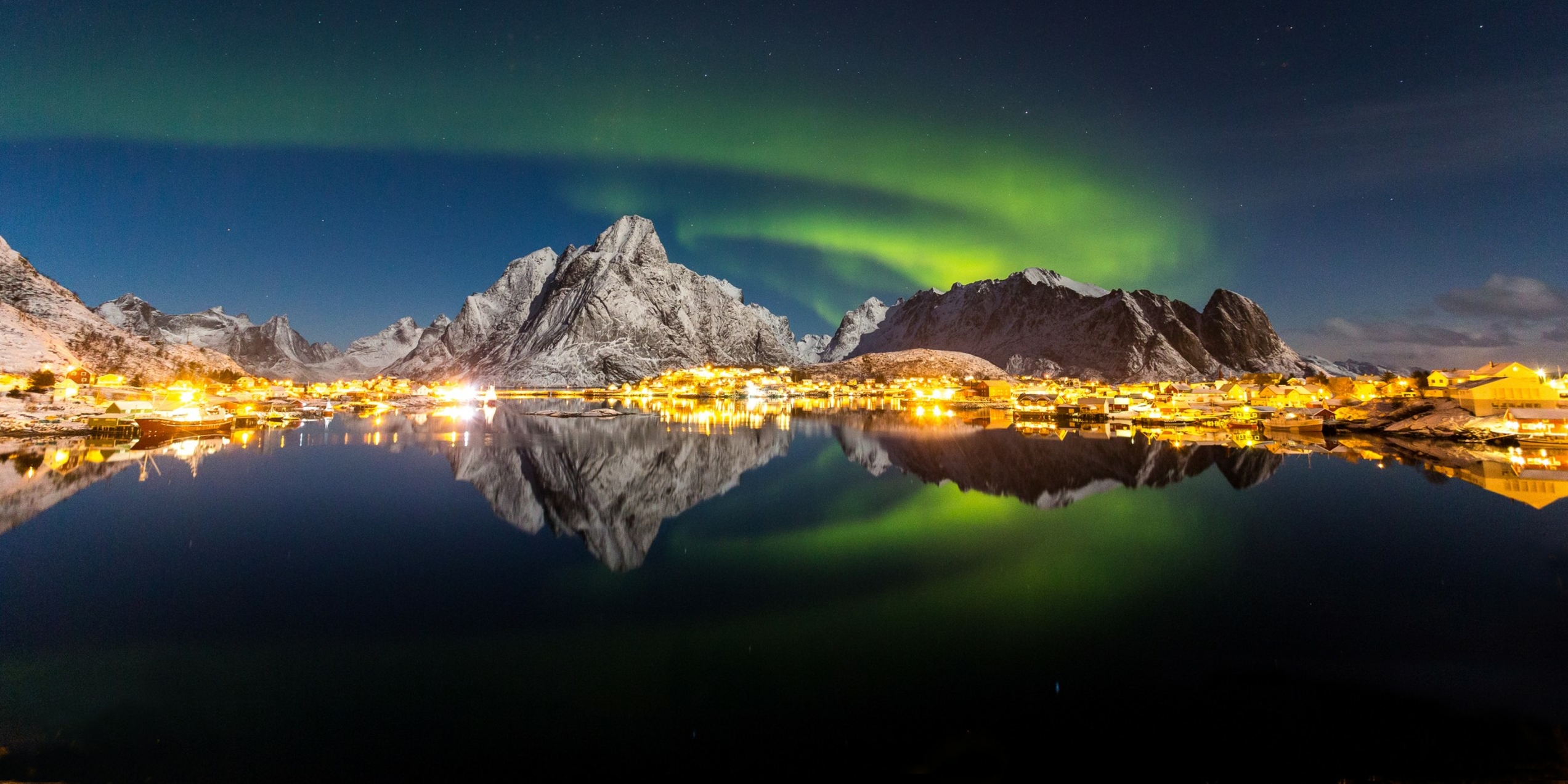 Northern lights over snow covered mountains, ocean and a city