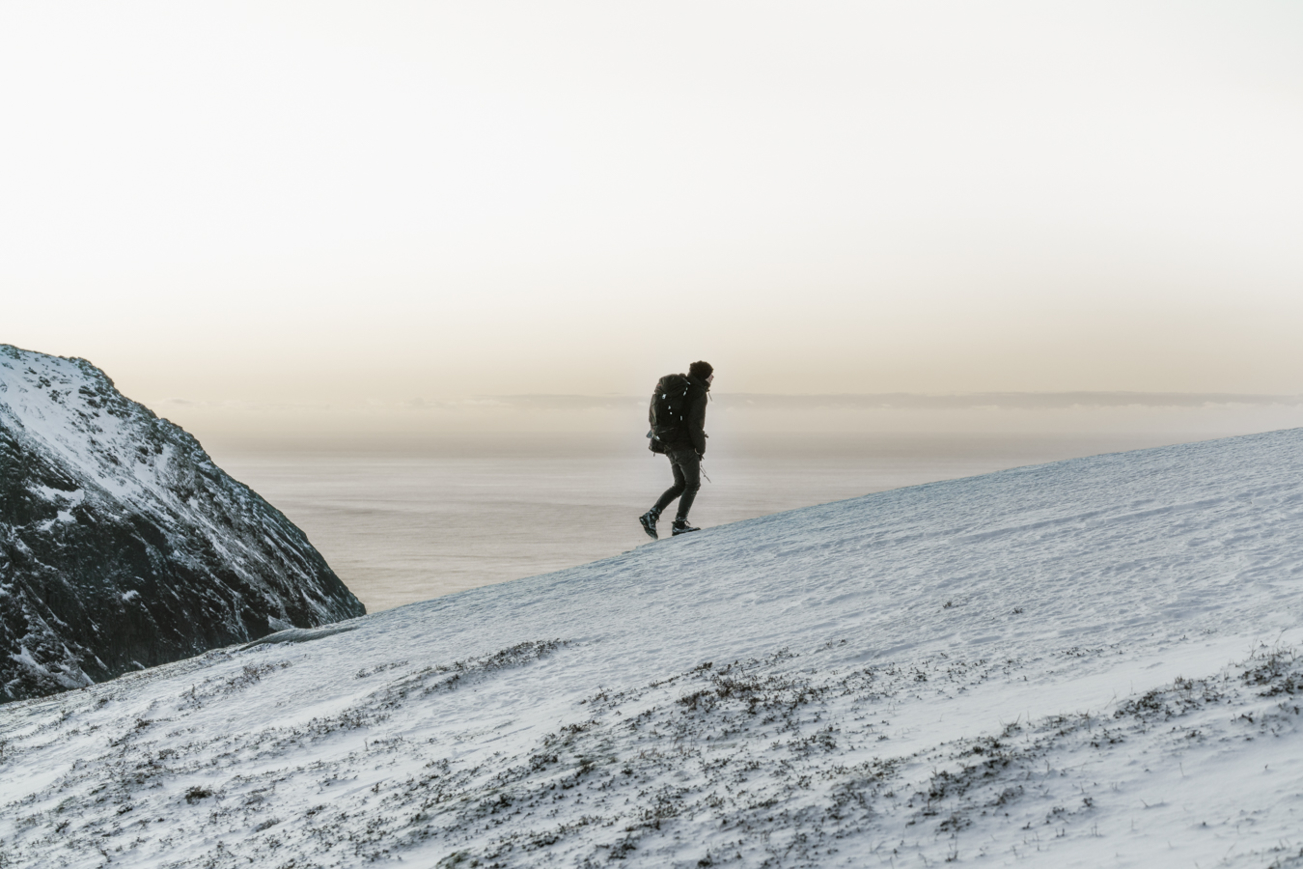 Person walking up a frozen mountain with the ocean behind