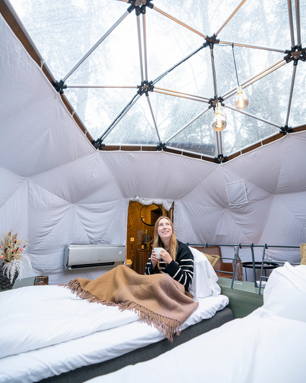Person sitting inside a dome-tent with a blanket and coffee