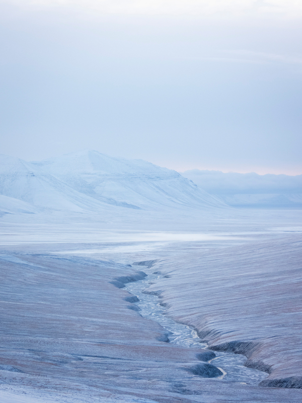 A snowcovered area with a frozen river and mountains, looking like a desert