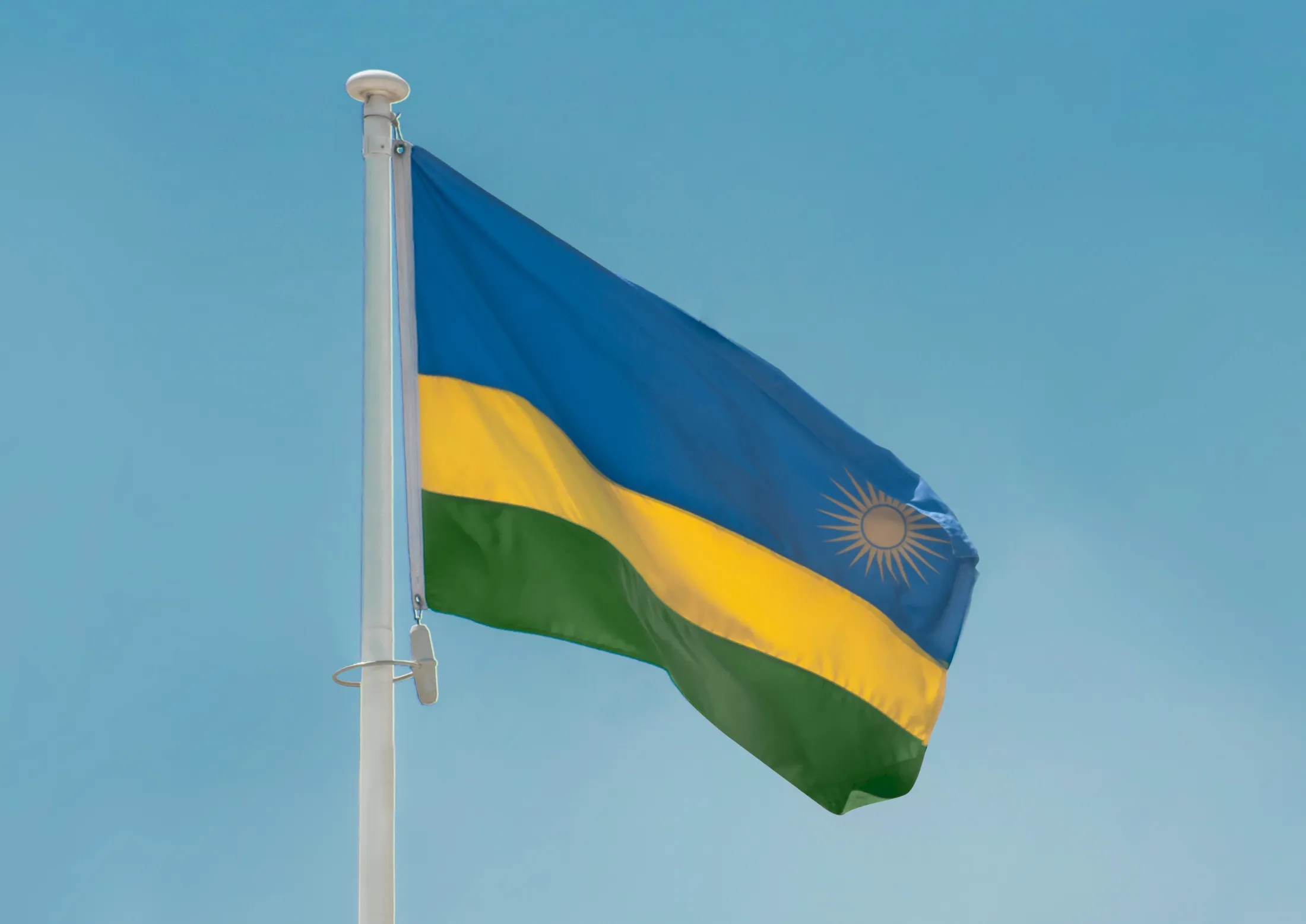 Rwandas flagg vaier mot en blå himmel.