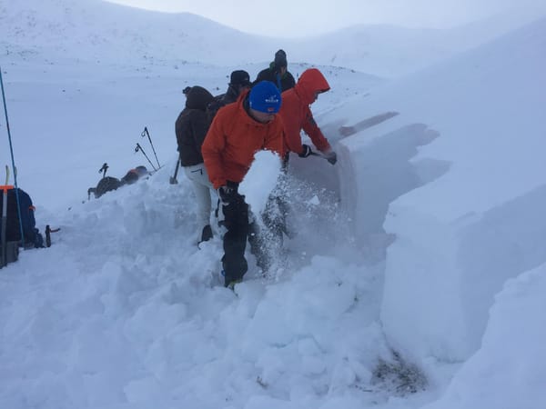 Personer i vinterklær graver i et snødekt fjellandskap.
