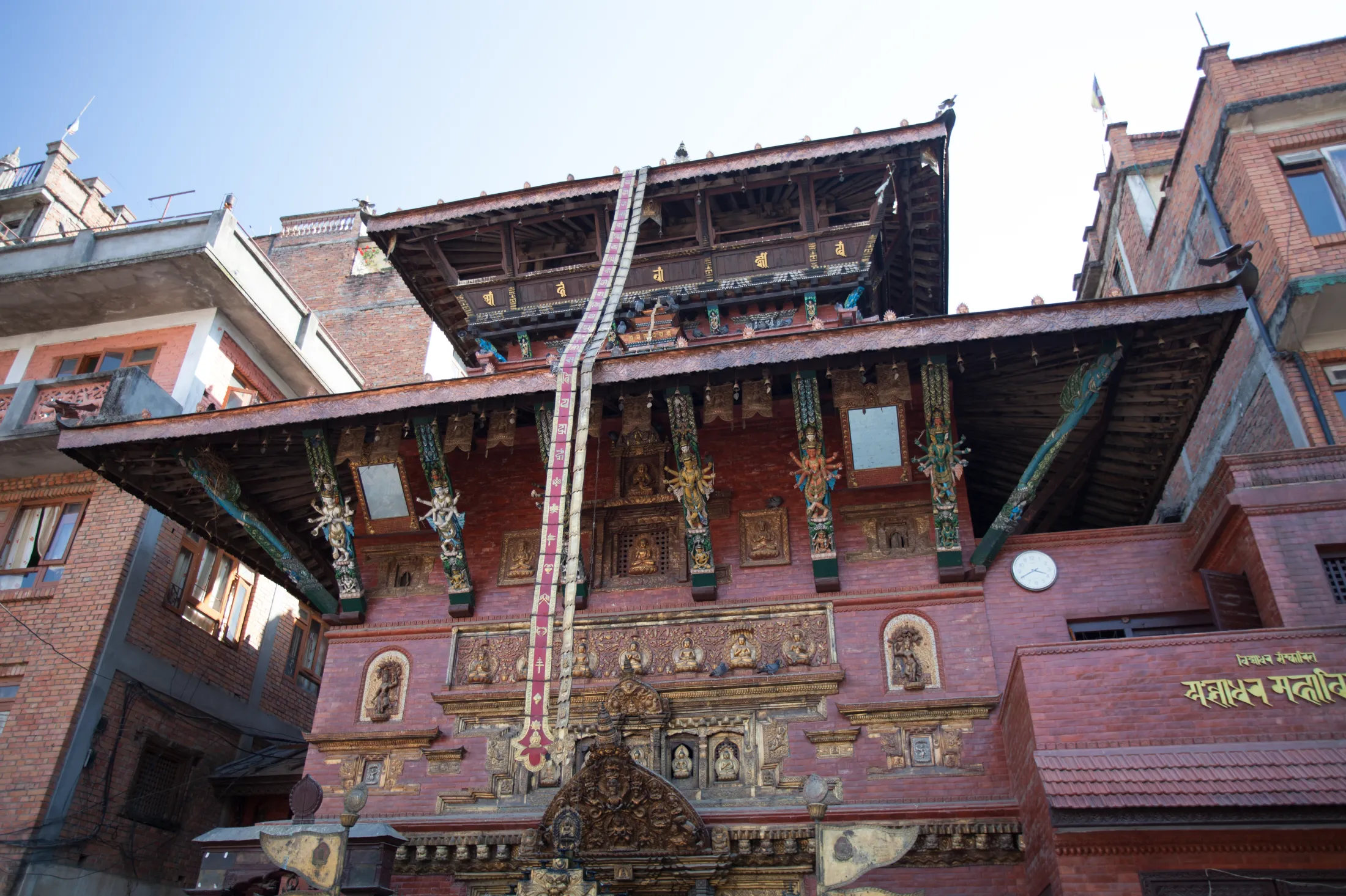 Et tradisjonelt Newari-tempel i flere etasjer, bygget av rød murstein og mørkt tre, har forseggjorte gullelementer, fargerike statuer på søylene og et langt, dekorativt bånd som henger fra det øverste taket.