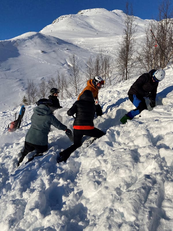 Flere skiløpere som øver på kameratredning ved skred i et fjellandskap dekket av snø.