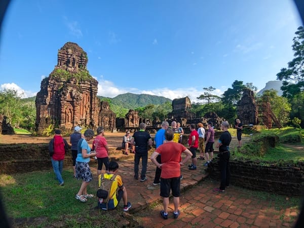 En gruppe turister som utforsker de gamle ruinene av My Son-helligdommen i Vietnam under en klar blå himmel.