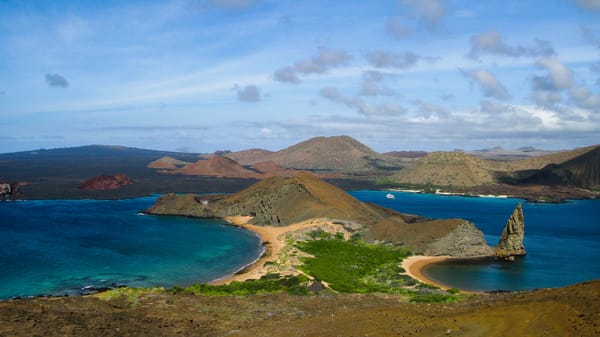 En opphøyd panoramautsikt over Bartolomé-øya på Galapagos, som viser Sullivan Bay, halvmåneformede sandstrender og den ikoniske Pinnacle Rock som reiser seg fra det dypblå havet.