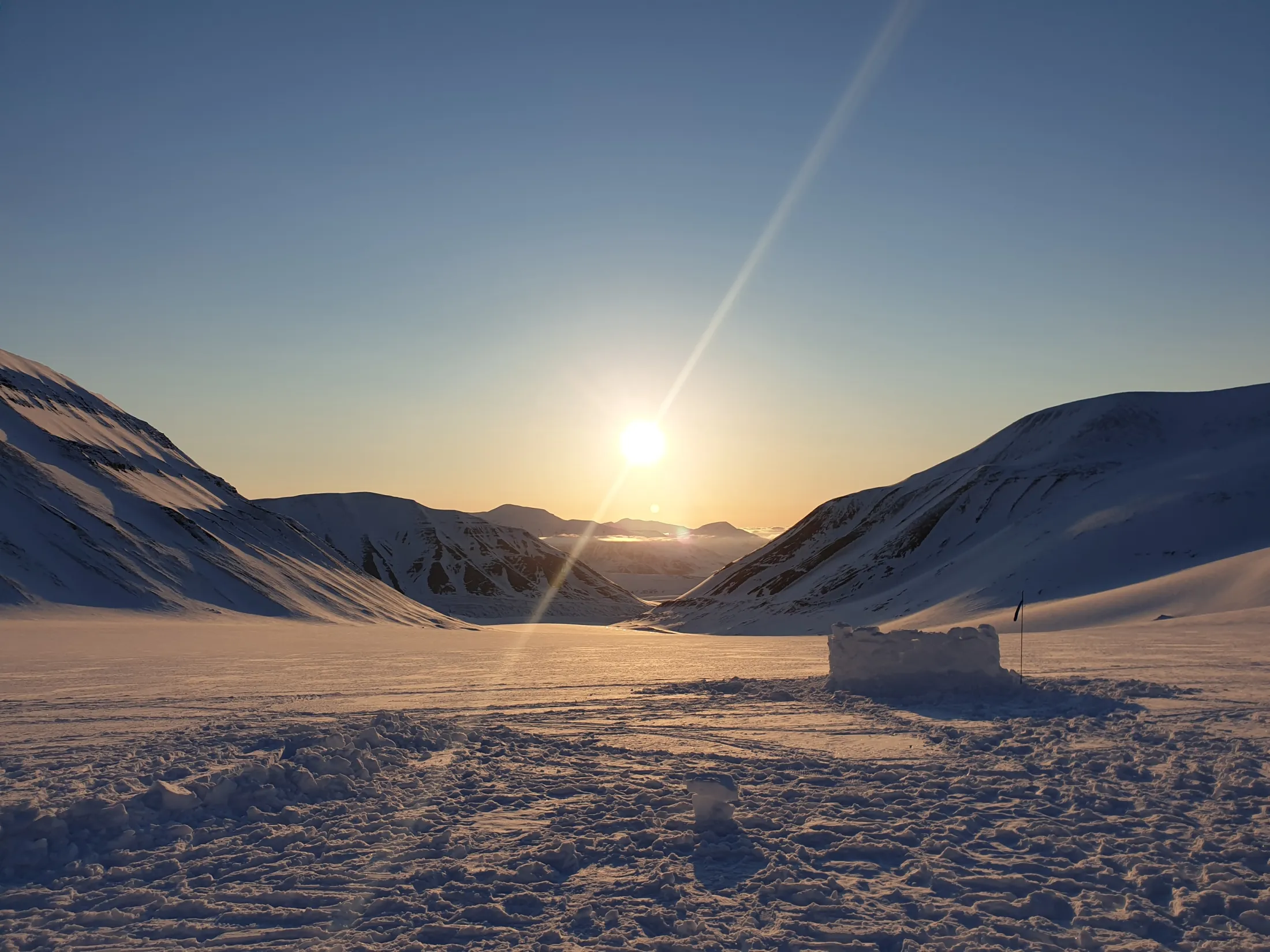 Et snølandskap med fjell under en sterk sol, med en solstråle på skrå over himmelen.