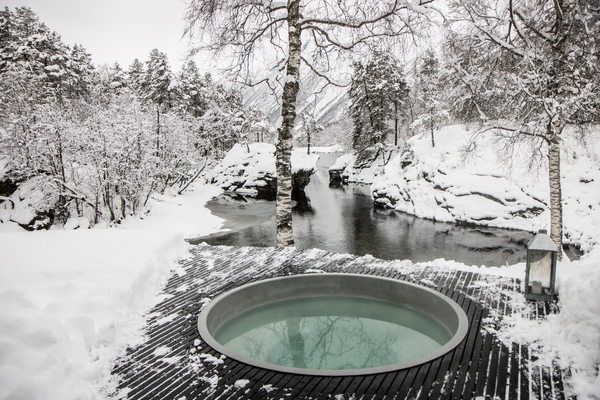 Et utendørs badestamp i et snødekt vinterlandskap med elv og trær i bakgrunnen.