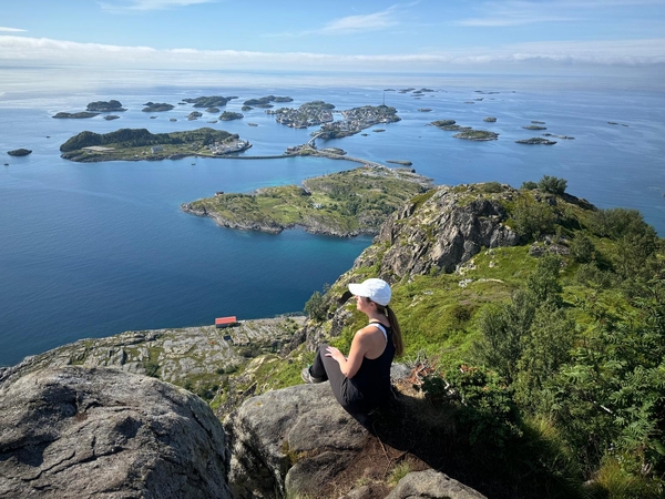 En turgåer sitter på en fjelltopp med utsikt over et landskap med øyer i havet.
