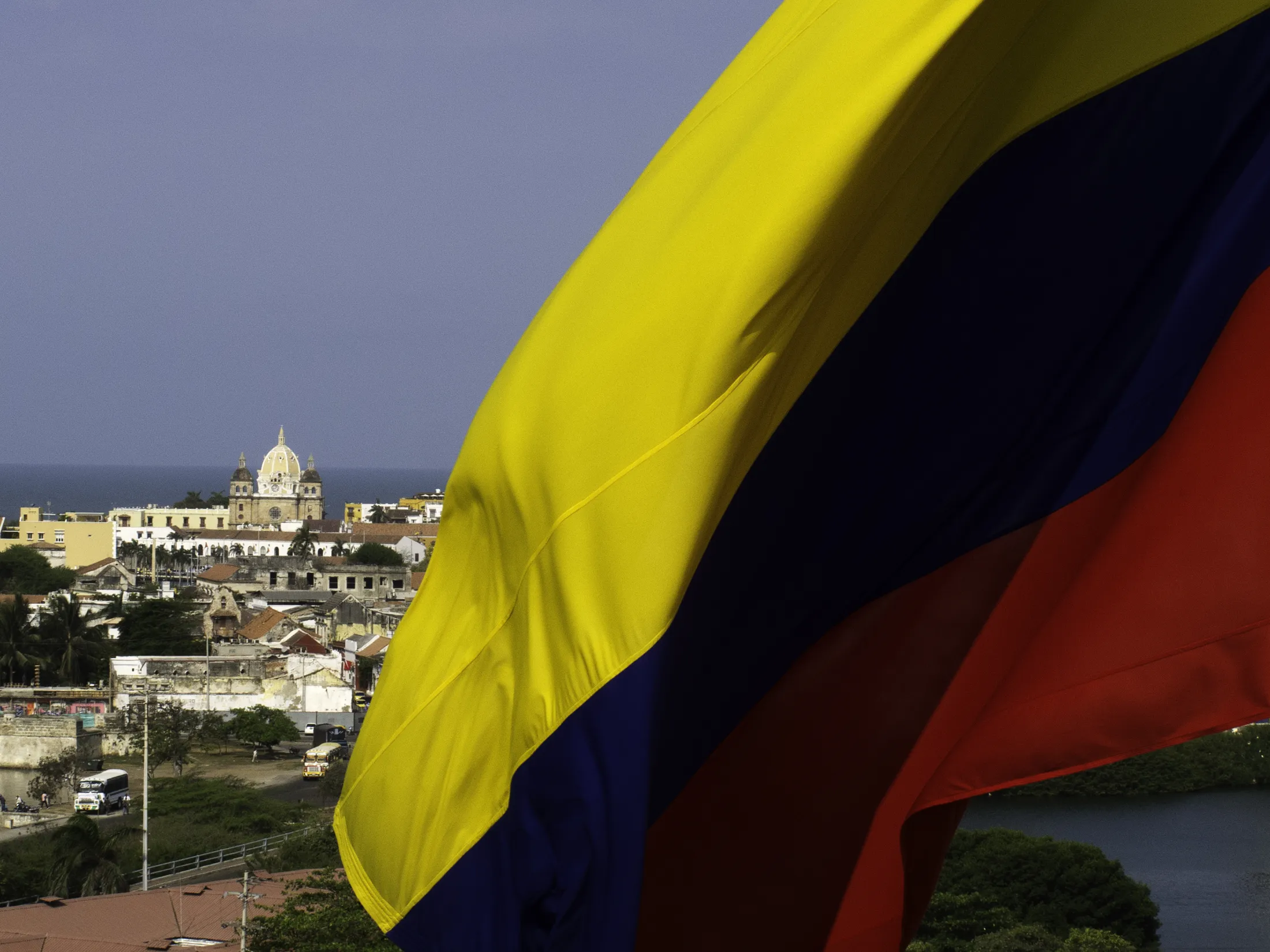 Det colombianske flagget vaier med utsikt over en by og havet i bakgrunnen.