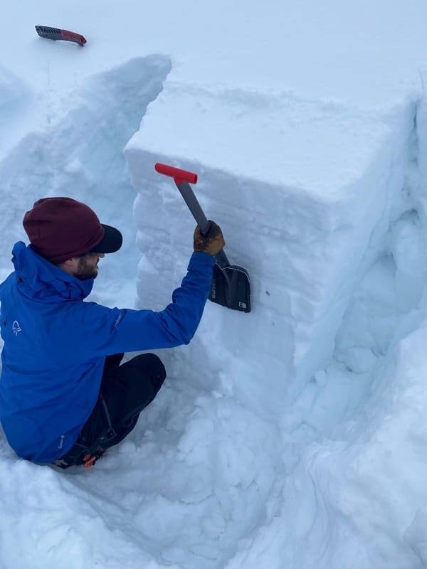 En person i blå jakke bruker en spade til å banke på en stor snøblokk under en stabilitetstest for snøskred.