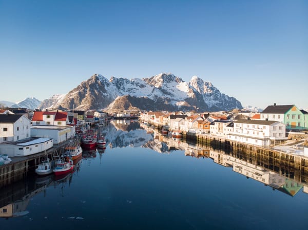 En havn i Norge med fargerike hus og snødekte fjell som speiler seg i det rolige vannet.