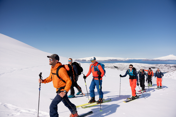 En gruppe mennesker som går på topptur i et snødekt fjell under en blå himmel.