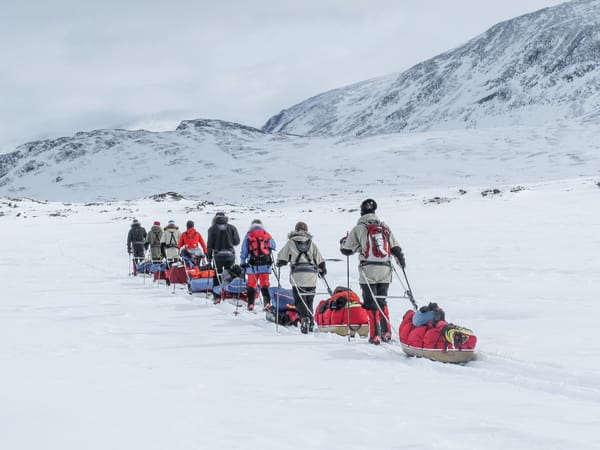En gruppe mennesker krysser et snølandskap og trekker pulker med utstyr.